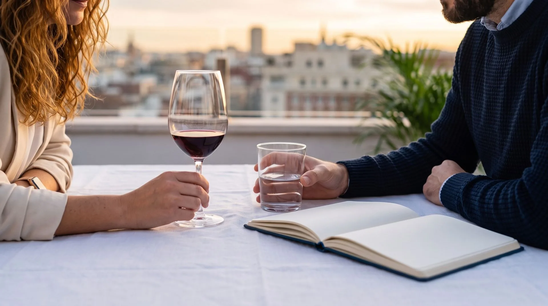 Dos personas conversan en una terraza de Madrid al atardecer, con copas y un cuaderno abierto
